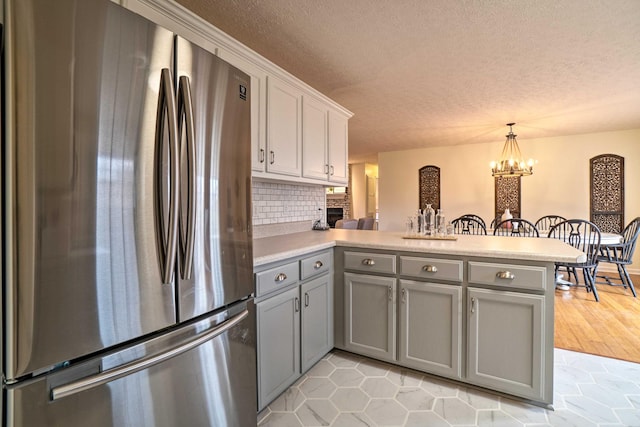 kitchen with freestanding refrigerator, gray cabinetry, a peninsula, a textured ceiling, and light countertops