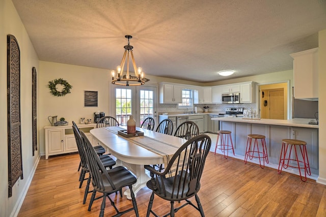 dining area featuring light wood-style flooring, a chandelier, a textured ceiling, and baseboards