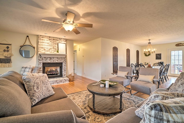 living room featuring a textured ceiling, a chandelier, light wood finished floors, ceiling fan, and a fireplace