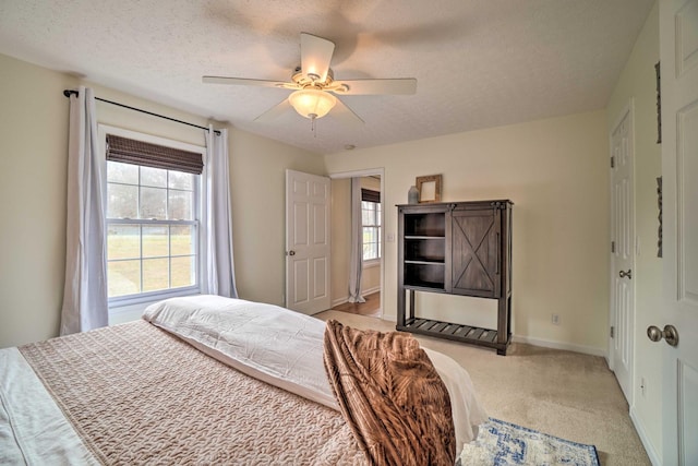 bedroom featuring a textured ceiling, light colored carpet, baseboards, and ceiling fan