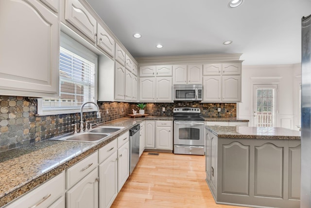 kitchen featuring stainless steel appliances, a sink, plenty of natural light, light wood finished floors, and ornamental molding