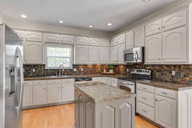 kitchen featuring stainless steel appliances, a sink, light wood-type flooring, a kitchen island, and ornamental molding