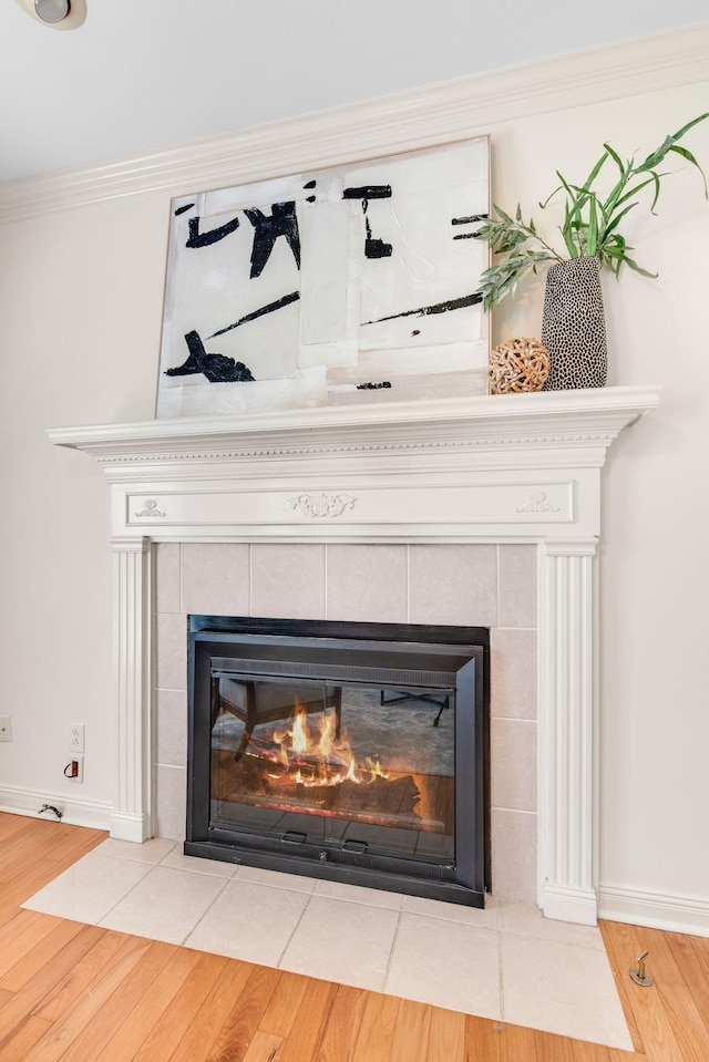 detailed view of a fireplace, wood finished floors, baseboards, and crown molding
