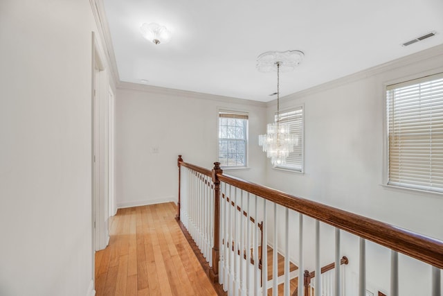 hallway with a chandelier, ornamental molding, light wood-type flooring, baseboards, and an upstairs landing