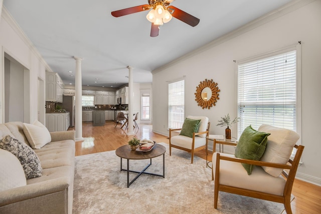 living room with ornate columns, crown molding, light wood-type flooring, ceiling fan, and baseboards
