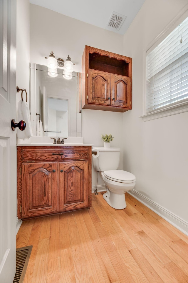 half bathroom featuring wood finished floors, toilet, baseboards, and vanity
