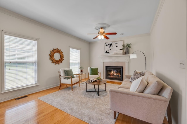 living room featuring a tiled fireplace, wood finished floors, crown molding, ceiling fan, and baseboards