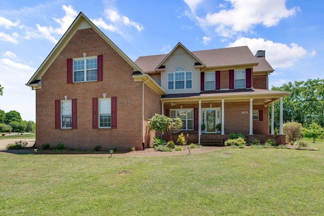 view of front of home with a chimney, a front yard, brick siding, and a porch