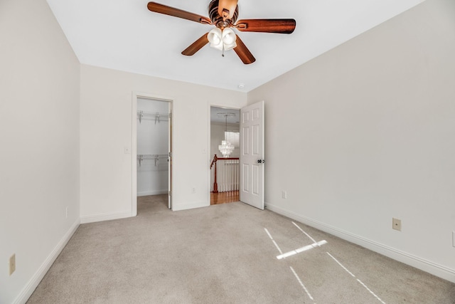 unfurnished bedroom featuring light carpet, baseboards, a walk in closet, and a ceiling fan
