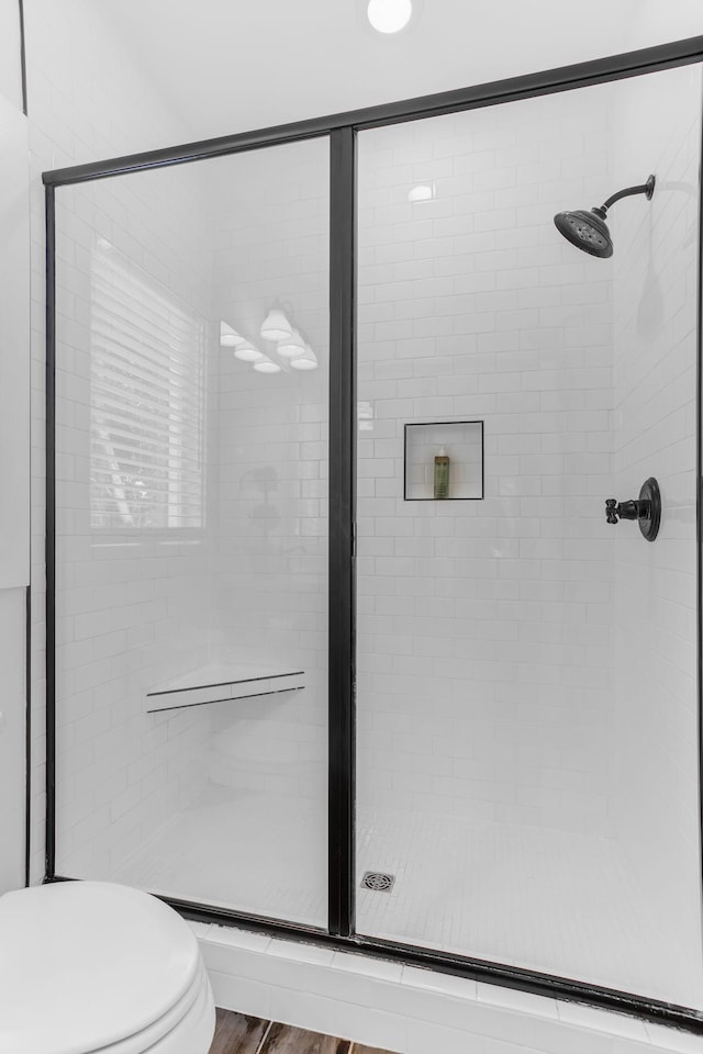 bathroom with a stall shower, toilet, and wood finished floors