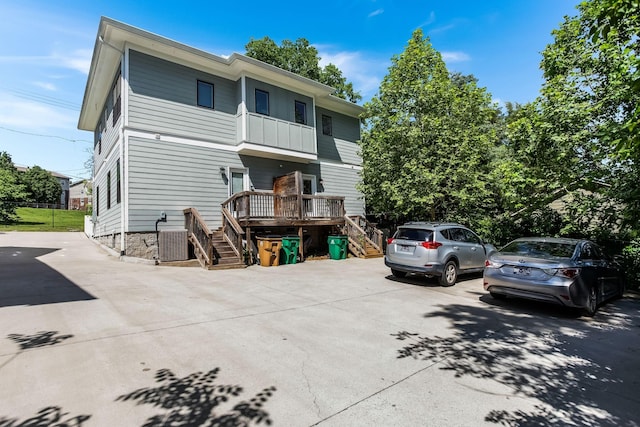 back of property featuring stairs, a balcony, central AC unit, and concrete driveway