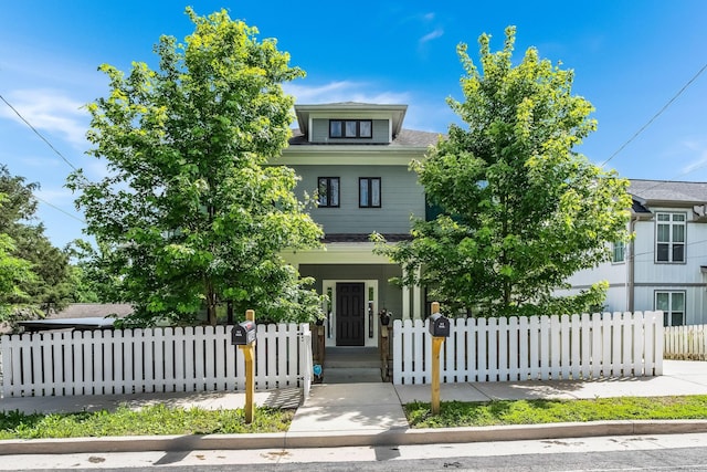 traditional style home with roof with shingles, a fenced front yard, and covered porch