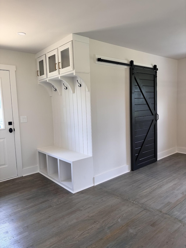 mudroom with a barn door, dark wood-type flooring, and baseboards