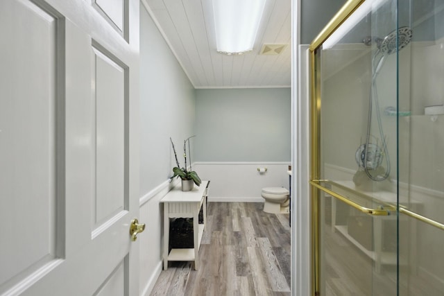bathroom with toilet, a shower stall, wood finished floors, ornamental molding, and a wainscoted wall