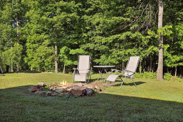 view of grassy yard with a fire pit and a wooded view