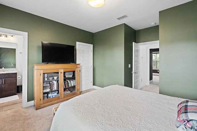 bedroom with light carpet, baseboards, and ensuite bath