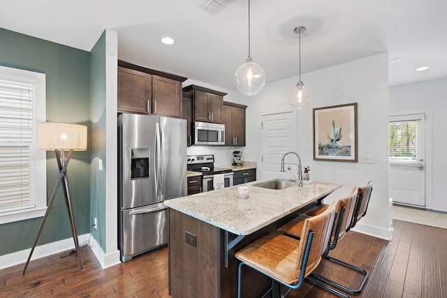 kitchen featuring appliances with stainless steel finishes, a sink, baseboards, dark brown cabinets, and light stone counters