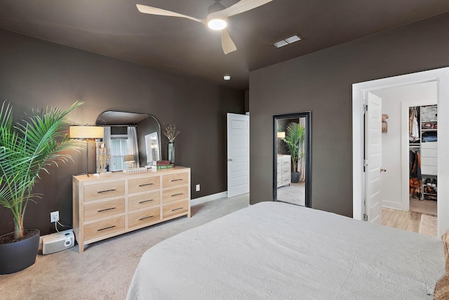 bedroom featuring light colored carpet, ceiling fan, baseboards, and a walk in closet