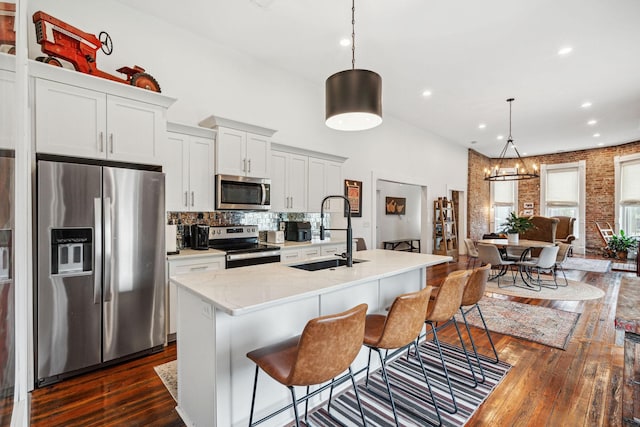 kitchen with appliances with stainless steel finishes, a sink, dark wood-type flooring, a center island with sink, and backsplash