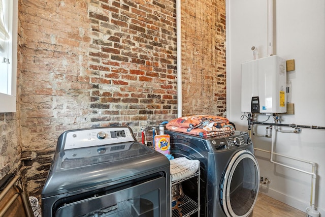laundry area featuring tankless water heater, washing machine and clothes dryer, baseboards, brick wall, and wood finished floors