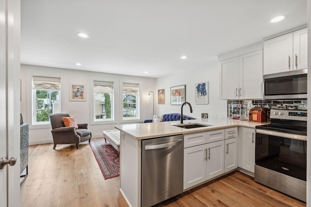 kitchen with appliances with stainless steel finishes, a sink, a peninsula, open floor plan, and light countertops