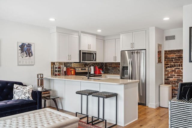 kitchen with appliances with stainless steel finishes, a peninsula, a kitchen bar, tasteful backsplash, and light wood finished floors