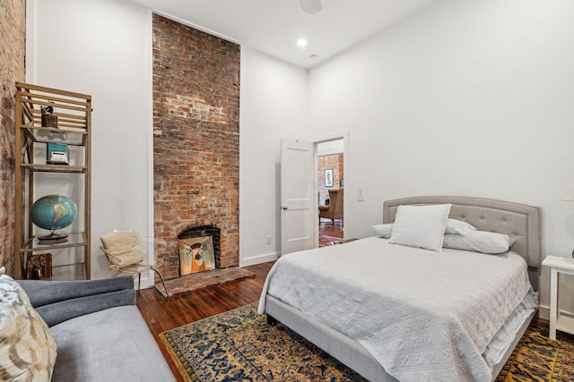 bedroom with wood finished floors, a high ceiling, a fireplace, baseboards, and recessed lighting