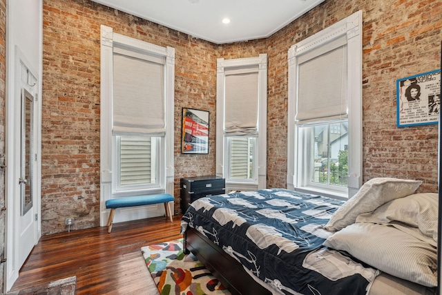 bedroom featuring brick wall and hardwood / wood-style flooring