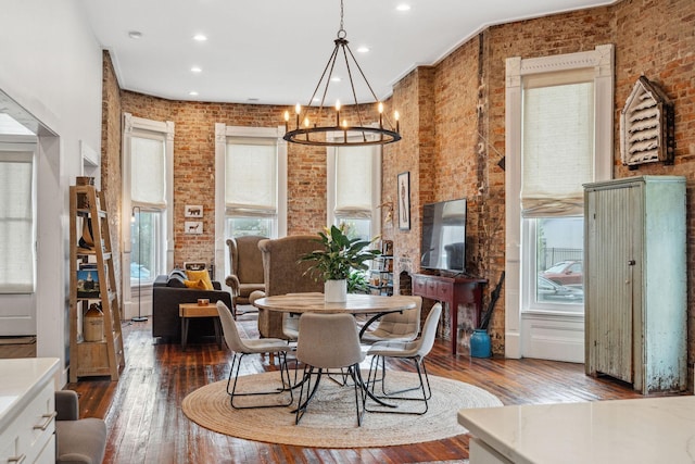 dining space with wood-type flooring, brick wall, a chandelier, and recessed lighting