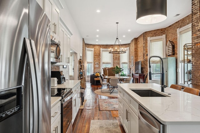 kitchen with appliances with stainless steel finishes, a sink, dark wood finished floors, a center island with sink, and white cabinetry