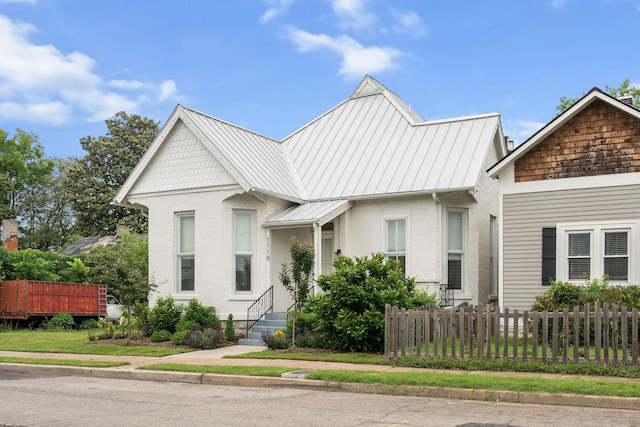view of front of property featuring a standing seam roof, fence, metal roof, and brick siding