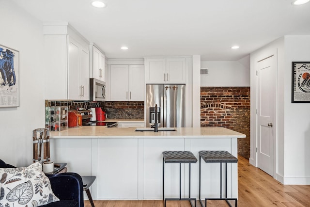 kitchen with appliances with stainless steel finishes, a peninsula, light countertops, light wood-style floors, and a breakfast bar