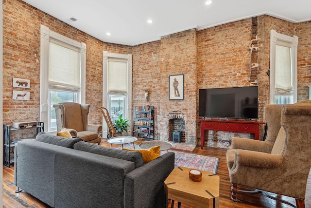 living area featuring wood finished floors, a fireplace, brick wall, and recessed lighting