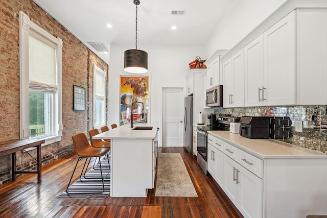 kitchen featuring appliances with stainless steel finishes, a sink, white cabinets, a kitchen island with sink, and dark wood-style floors