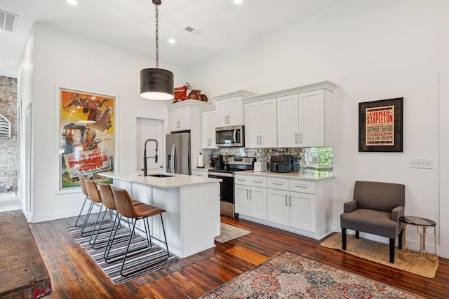 kitchen featuring appliances with stainless steel finishes, a sink, dark wood finished floors, a kitchen breakfast bar, and decorative backsplash