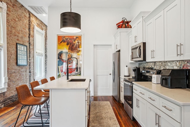 kitchen with appliances with stainless steel finishes, a sink, dark wood-style floors, a kitchen island with sink, and a breakfast bar