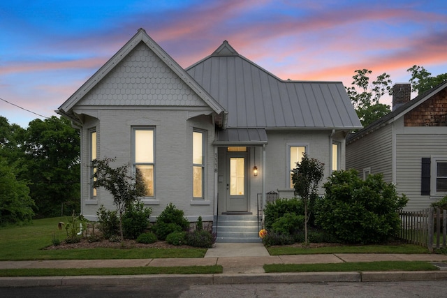 view of front facade with brick siding, fence, and a standing seam roof