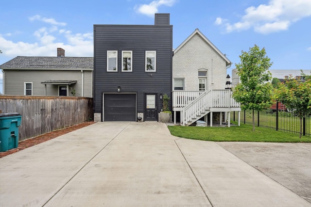 rear view of house with concrete driveway, an attached garage, a chimney, and stairs