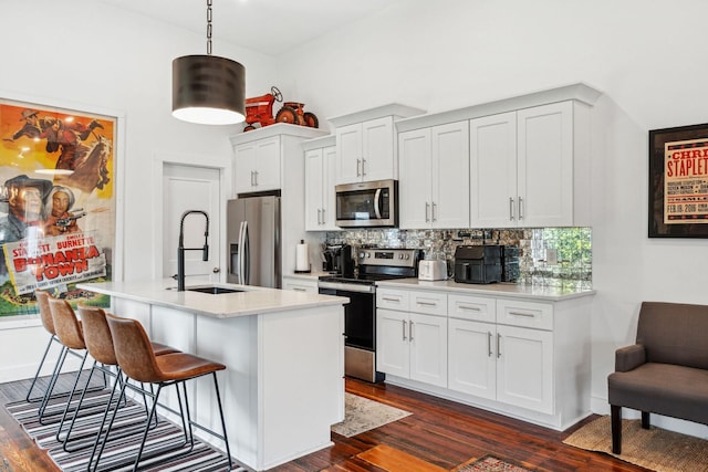 kitchen featuring appliances with stainless steel finishes, a sink, dark wood finished floors, decorative backsplash, and light countertops