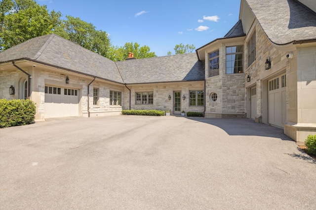 view of front of property with stone siding, an attached garage, driveway, and a chimney