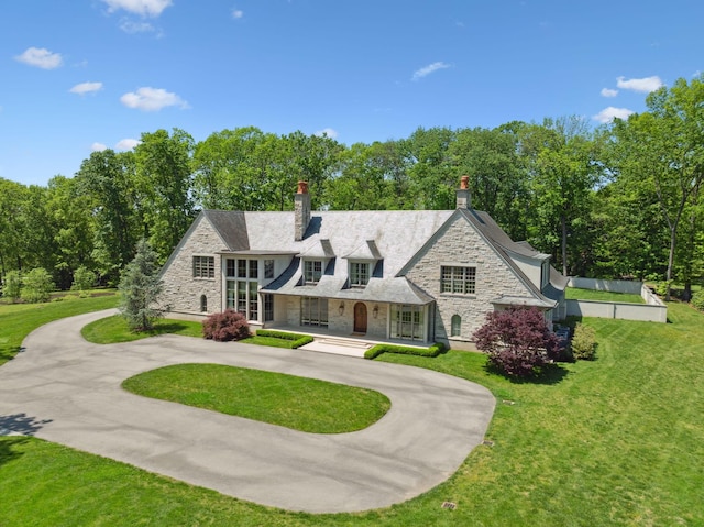 view of front of property with stone siding, a chimney, curved driveway, and a front lawn
