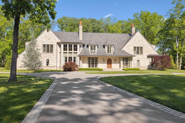 view of front of house with stone siding, a front lawn, and a chimney