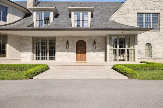 doorway to property with stone siding, a porch, and a chimney