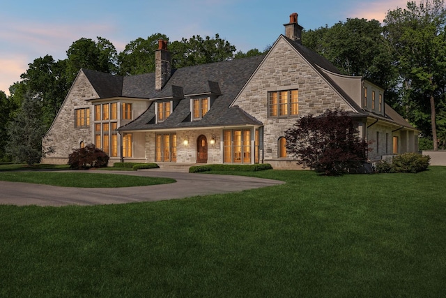 view of front of house with stone siding, a chimney, a yard, and curved driveway