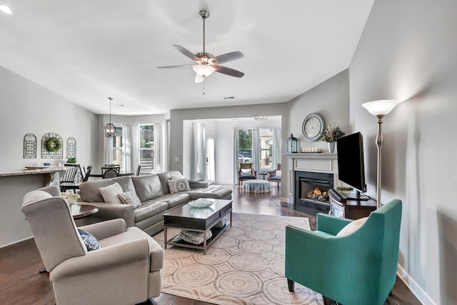 living room featuring wood finished floors, a fireplace with flush hearth, a ceiling fan, and baseboards