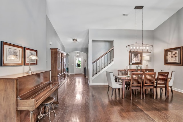 dining area with arched walkways, dark wood-style flooring, stairs, baseboards, and a towering ceiling