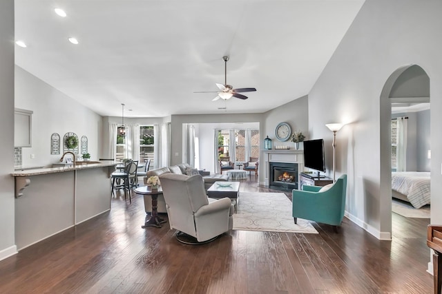 living room featuring a ceiling fan, dark wood-style flooring, recessed lighting, baseboards, and a lit fireplace