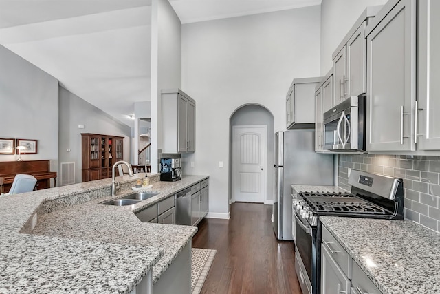 kitchen featuring appliances with stainless steel finishes, a sink, gray cabinetry, light stone counters, and high vaulted ceiling
