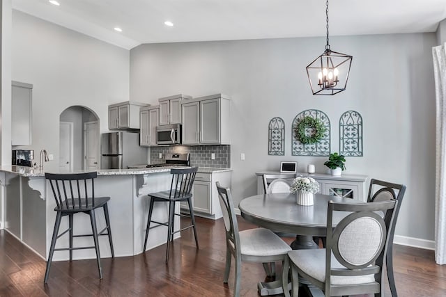 dining room with high vaulted ceiling, a chandelier, arched walkways, dark wood finished floors, and baseboards