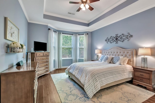 bedroom with dark wood finished floors, a tray ceiling, crown molding, and ceiling fan